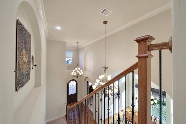 hallway featuring a chandelier, a high ceiling, visible vents, baseboards, and crown molding