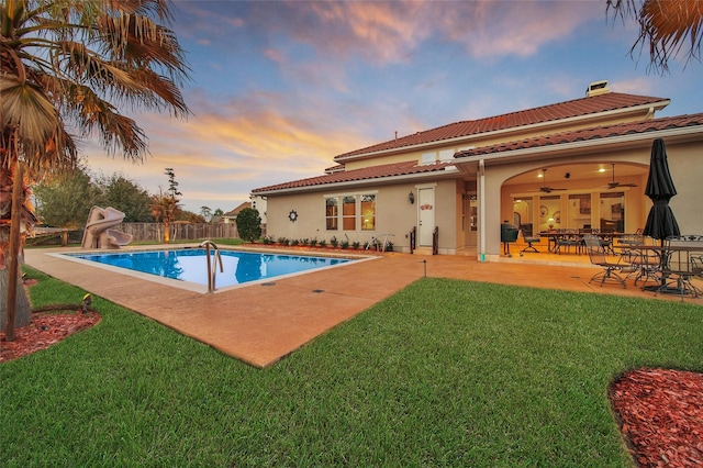 pool at dusk featuring a yard, a water slide, a patio, and a fenced in pool