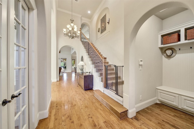 mudroom with crown molding, arched walkways, a notable chandelier, and light wood-style flooring