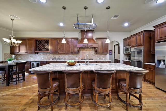 kitchen featuring arched walkways, stainless steel appliances, visible vents, and a large island with sink