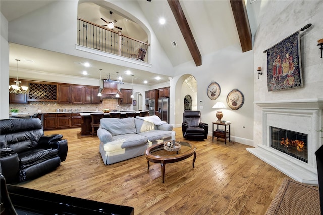 living area with arched walkways, light wood-style flooring, a glass covered fireplace, high vaulted ceiling, and beamed ceiling