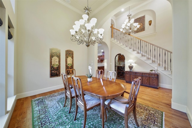 dining space with a chandelier, arched walkways, wood finished floors, a towering ceiling, and crown molding