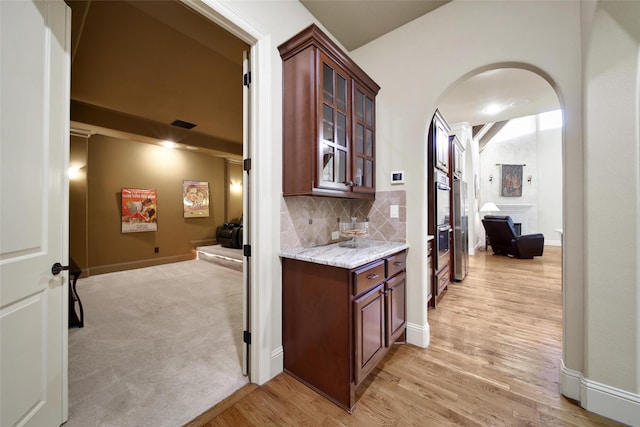 bar featuring arched walkways, decorative backsplash, baseboards, light wood-style flooring, and double oven