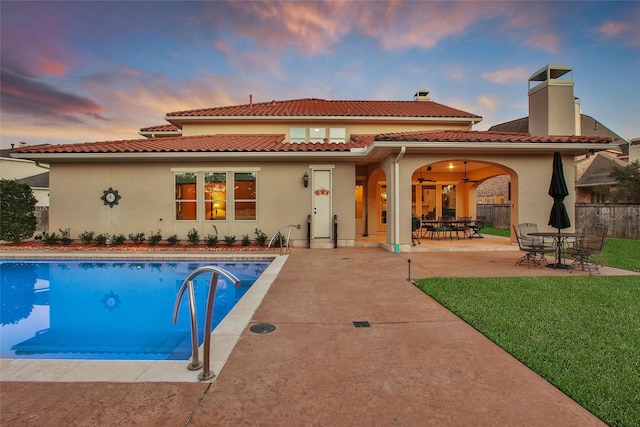 back of property with a fenced in pool, a tiled roof, fence, a patio area, and stucco siding