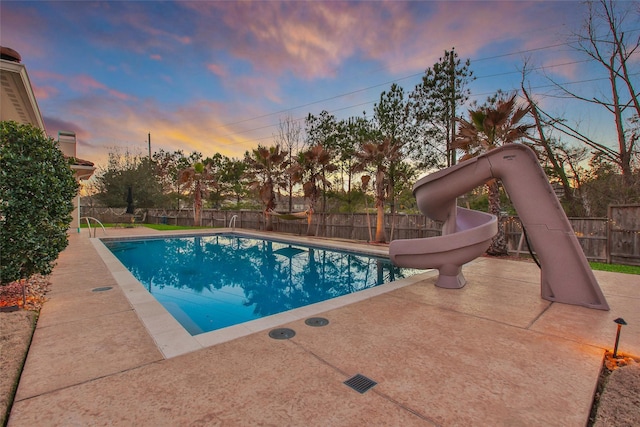 pool at dusk featuring a water slide, a fenced backyard, and a fenced in pool