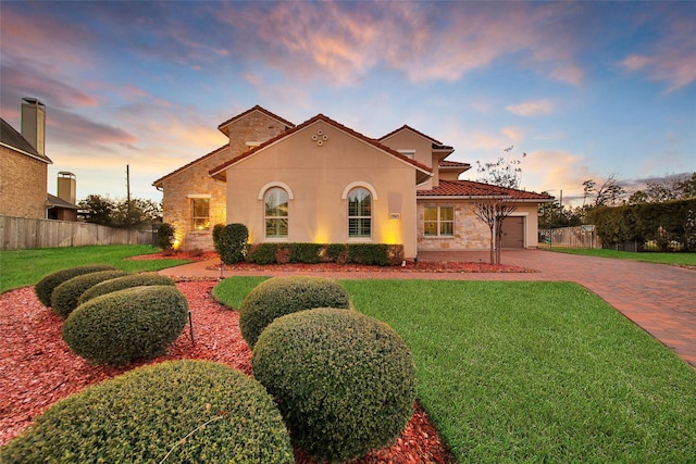 mediterranean / spanish house with decorative driveway, a yard, fence, a garage, and a tiled roof