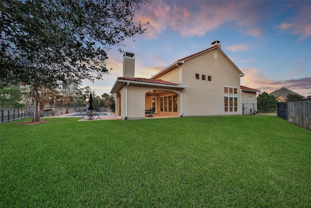 back of property with a yard, a chimney, a patio area, and a fenced backyard