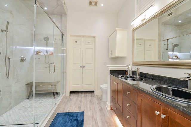 bathroom featuring double vanity, visible vents, toilet, a shower stall, and a sink