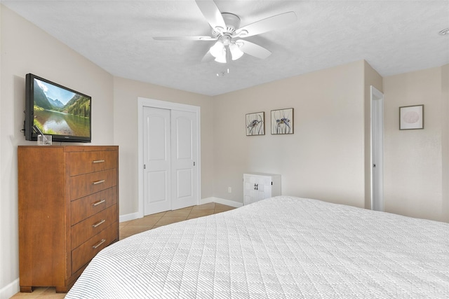 bedroom with light tile patterned floors, a closet, ceiling fan, a textured ceiling, and baseboards