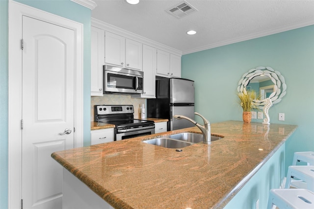 kitchen featuring appliances with stainless steel finishes, a peninsula, a kitchen bar, white cabinetry, and a sink