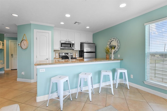 kitchen featuring visible vents, appliances with stainless steel finishes, a breakfast bar, a peninsula, and white cabinetry