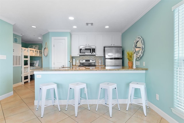 kitchen with visible vents, white cabinets, appliances with stainless steel finishes, a breakfast bar, and a peninsula