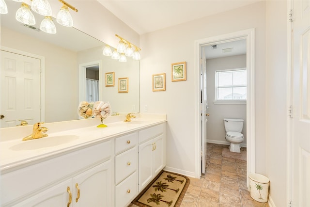 bathroom featuring double vanity, a sink, toilet, and baseboards