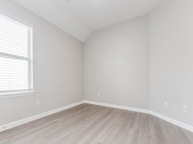 spare room with light wood-type flooring, lofted ceiling, and baseboards