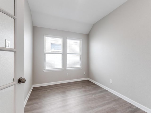 spare room featuring lofted ceiling, light wood-style flooring, and baseboards