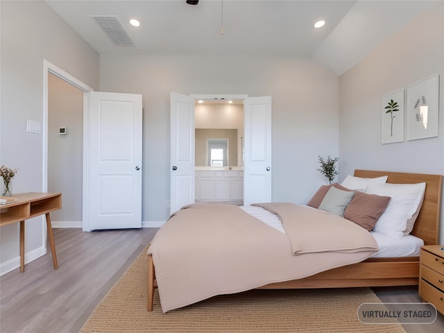 bedroom featuring light wood finished floors, visible vents, connected bathroom, vaulted ceiling, and baseboards