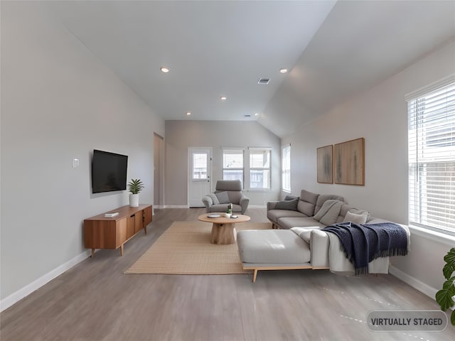 living area featuring light wood-type flooring, baseboards, vaulted ceiling, and a wealth of natural light