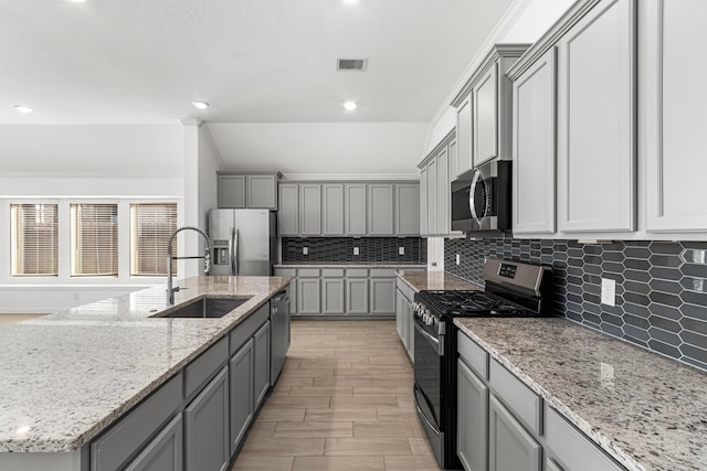 kitchen featuring light stone counters, stainless steel appliances, gray cabinets, a sink, and an island with sink