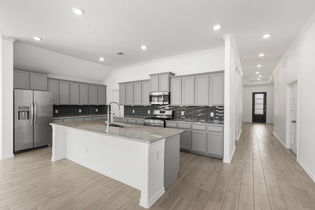 kitchen with gray cabinets, light stone countertops, a center island with sink, and stainless steel appliances