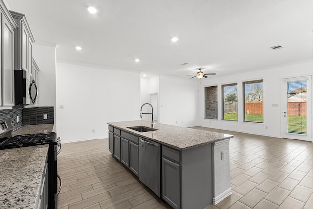 kitchen with appliances with stainless steel finishes, a kitchen island with sink, a sink, and light stone countertops