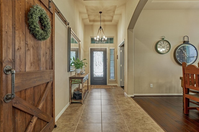 entrance foyer featuring arched walkways, a barn door, an inviting chandelier, wood finished floors, and baseboards