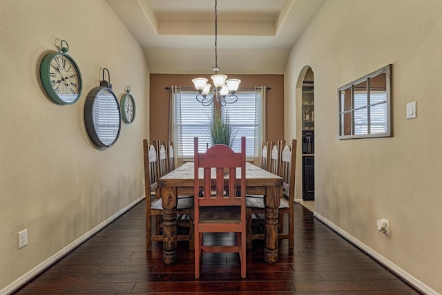 dining room featuring a tray ceiling, dark wood-style flooring, baseboards, and an inviting chandelier