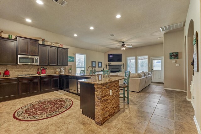 kitchen with light stone counters, stainless steel appliances, visible vents, a kitchen breakfast bar, and open floor plan