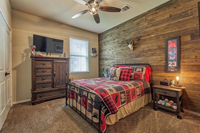 bedroom featuring a ceiling fan, visible vents, wood walls, and carpet flooring