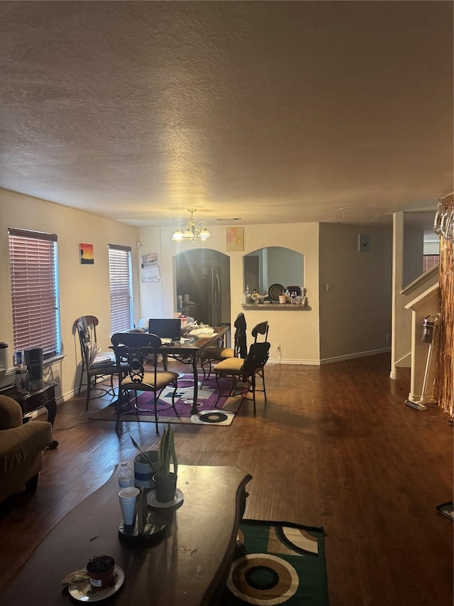 living area with a textured ceiling, dark wood-type flooring, baseboards, and an inviting chandelier