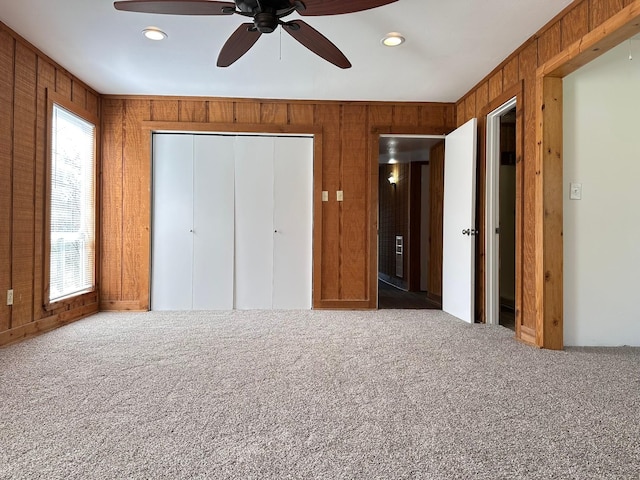 unfurnished bedroom featuring carpet floors, ceiling fan, wooden walls, and a closet