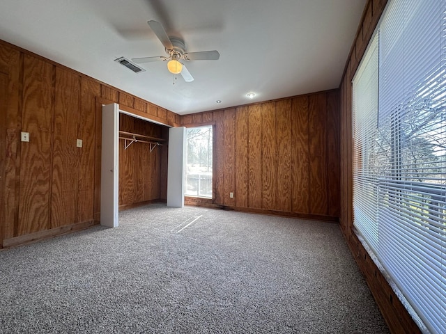 unfurnished bedroom with carpet floors, wood walls, a closet, and visible vents