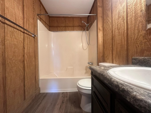 bathroom featuring toilet, washtub / shower combination, wood walls, vanity, and wood finished floors