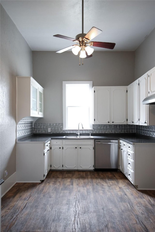 kitchen featuring dark countertops, backsplash, white cabinetry, a sink, and dishwasher