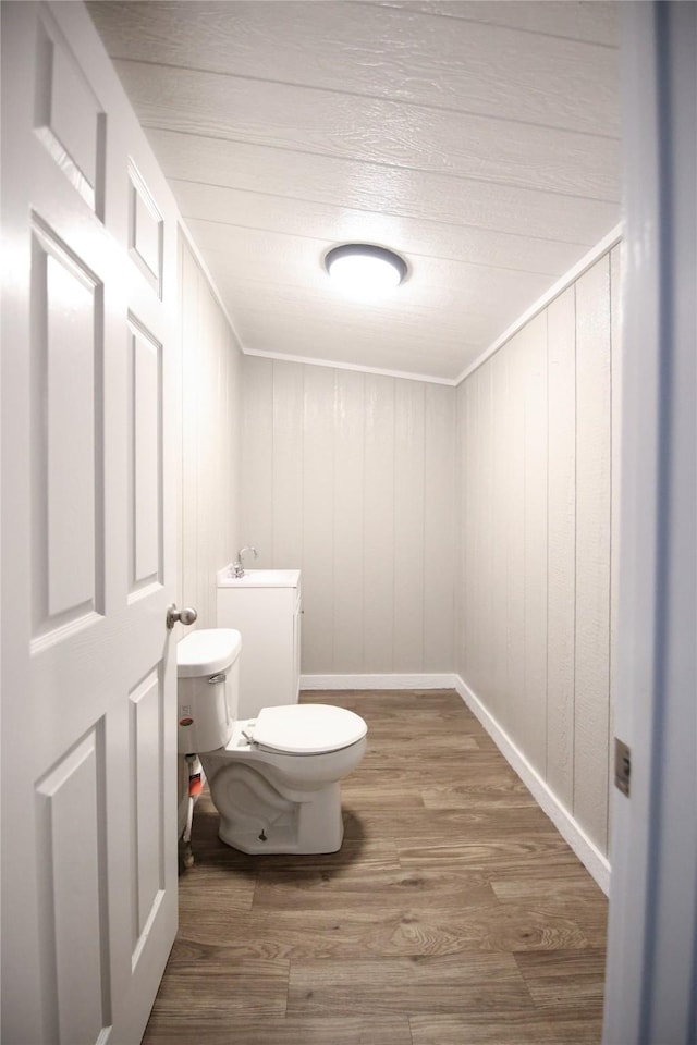 bathroom featuring toilet, a sink, ornamental molding, and wood finished floors