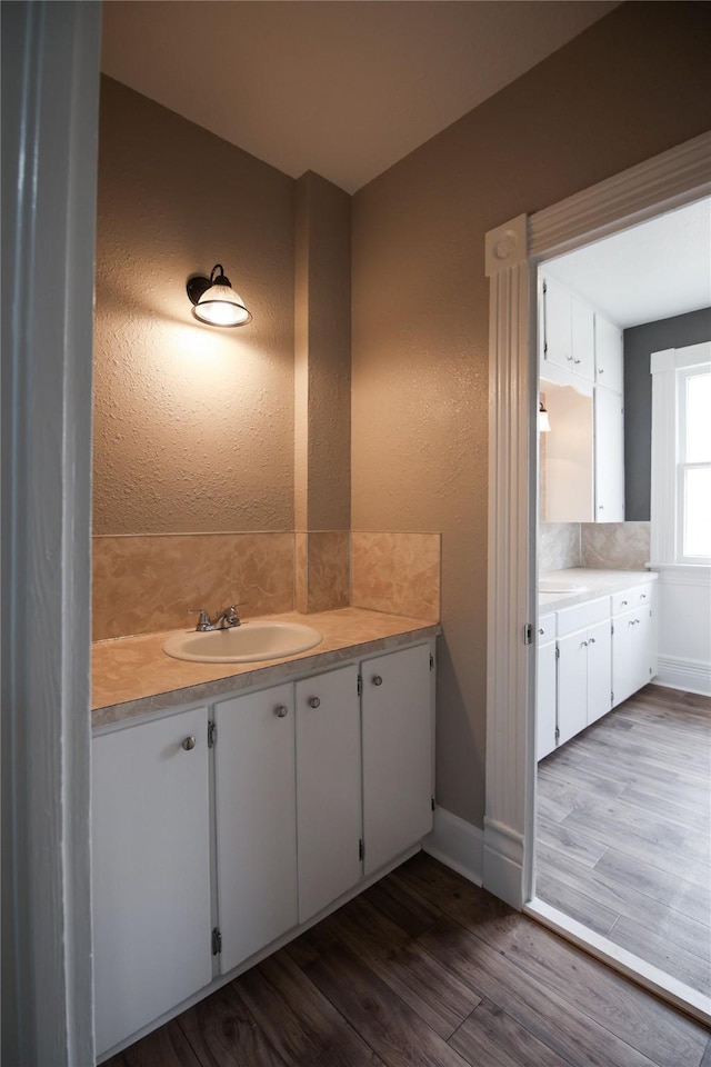 bathroom with a textured wall, vanity, baseboards, and wood finished floors