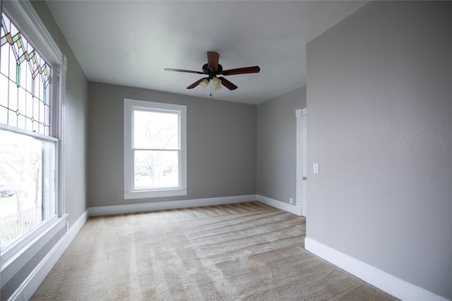 empty room with baseboards, a ceiling fan, and light colored carpet