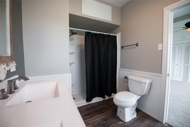 full bathroom with wainscoting, toilet, wood finished floors, a shower stall, and a sink