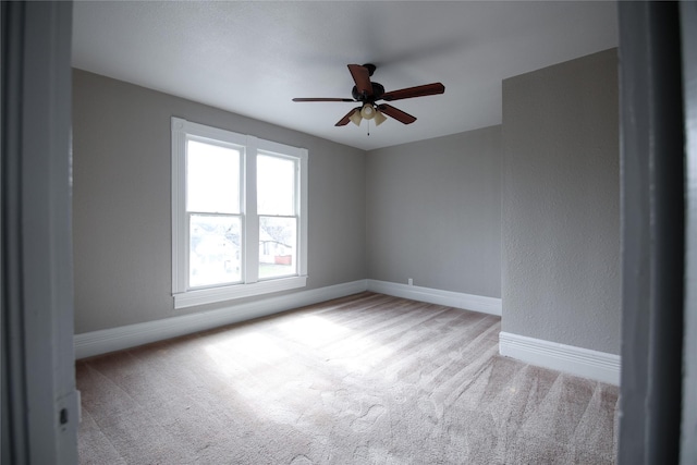 empty room with baseboards, a ceiling fan, and light colored carpet