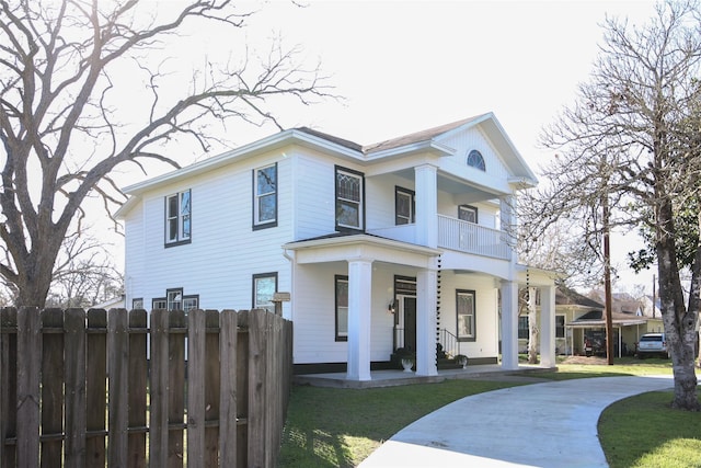 greek revival house with a porch, a front yard, fence, and a balcony