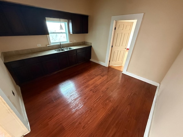 kitchen featuring light countertops, dark brown cabinetry, a sink, wood finished floors, and baseboards