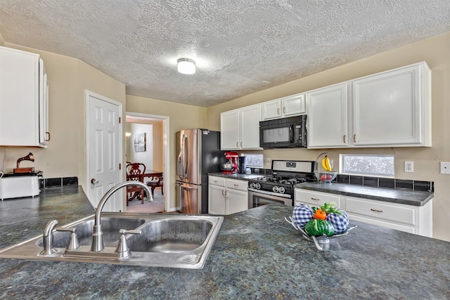 kitchen featuring dark countertops, white cabinets, stainless steel appliances, and a sink