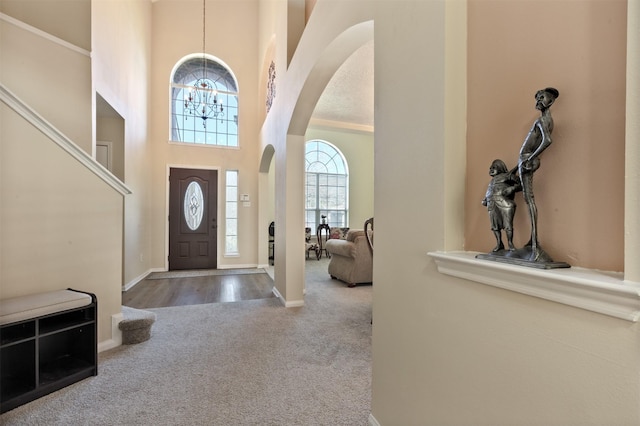 entrance foyer featuring arched walkways, a notable chandelier, a high ceiling, baseboards, and carpet