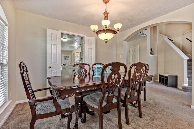 carpeted dining space featuring arched walkways, a textured ceiling, a notable chandelier, baseboards, and plenty of natural light