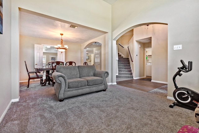 carpeted living room with arched walkways, a notable chandelier, washer / dryer, baseboards, and stairs