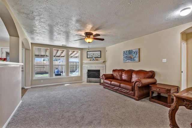 living area with carpet floors, arched walkways, a tiled fireplace, a ceiling fan, and baseboards