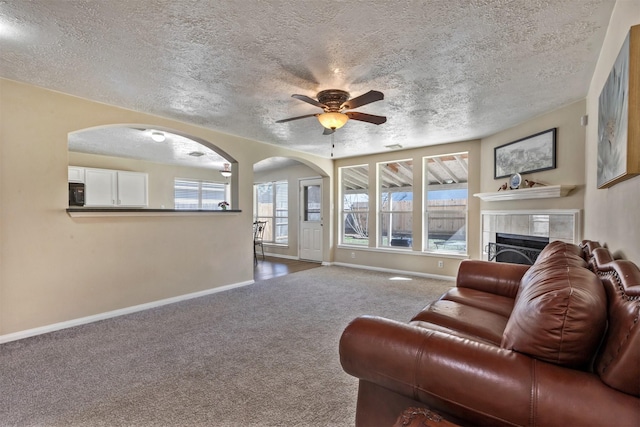 unfurnished living room featuring a tiled fireplace, a textured ceiling, carpet, and baseboards