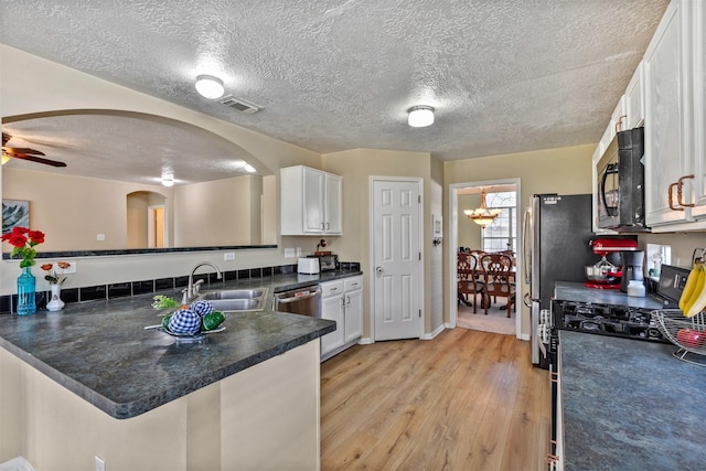 kitchen with dark countertops, appliances with stainless steel finishes, a peninsula, white cabinetry, and a sink