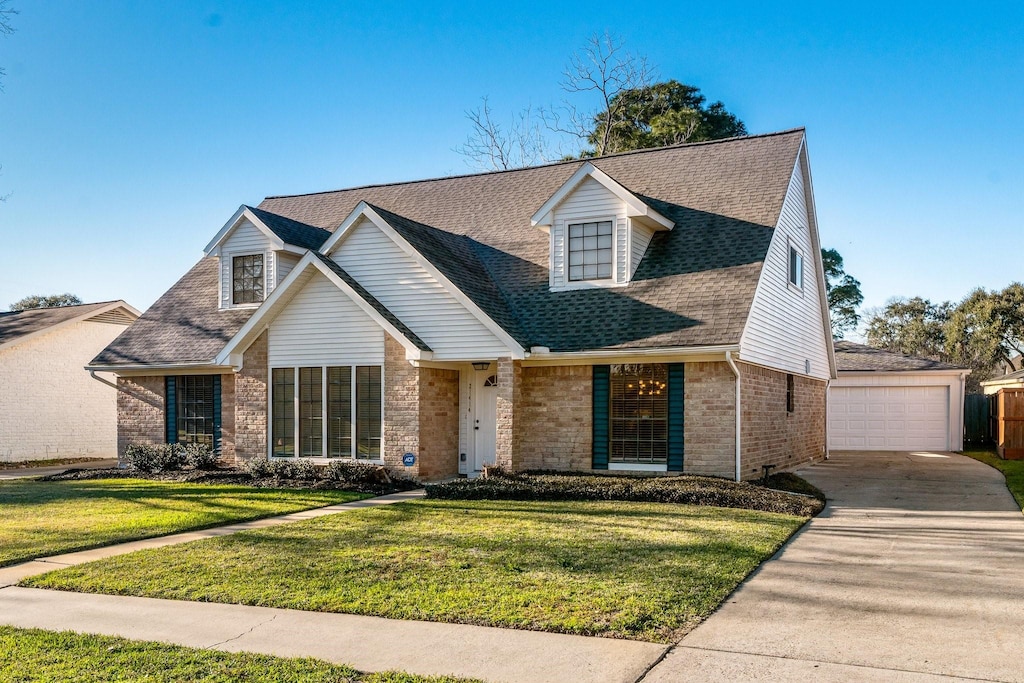 view of front of property featuring a front lawn, roof with shingles, a detached garage, and brick siding