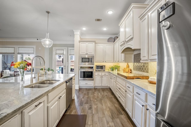 kitchen with appliances with stainless steel finishes, pendant lighting, a sink, and light stone counters