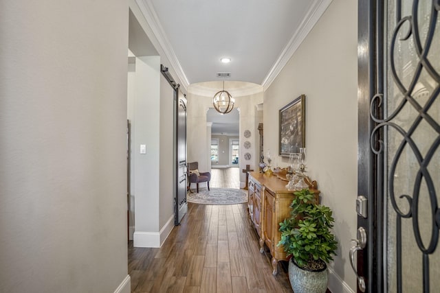 corridor with a barn door, dark wood-style flooring, visible vents, baseboards, and ornamental molding